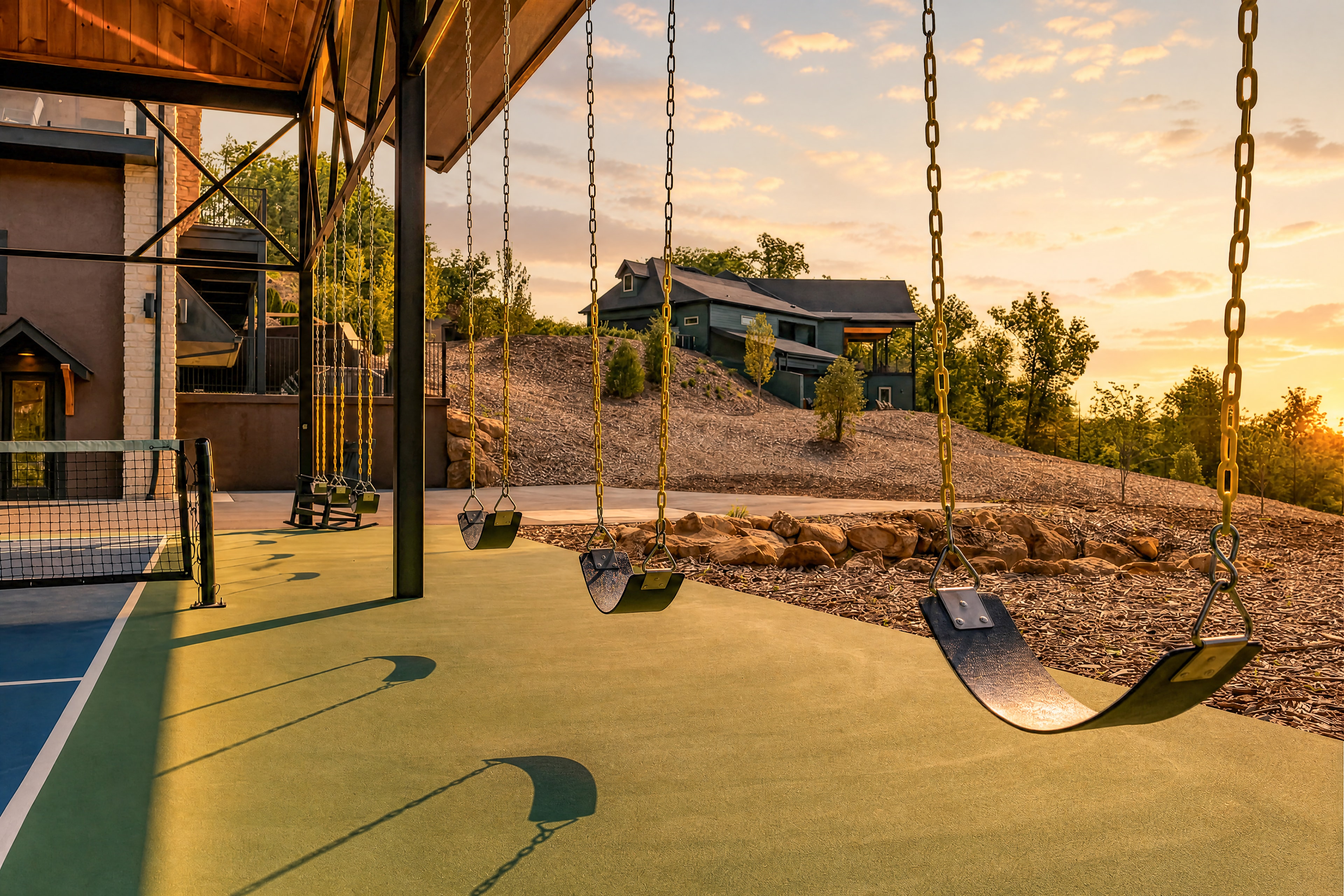 Swings beside the Excalibur pickleball court at golden hour, lodge and hillside in background