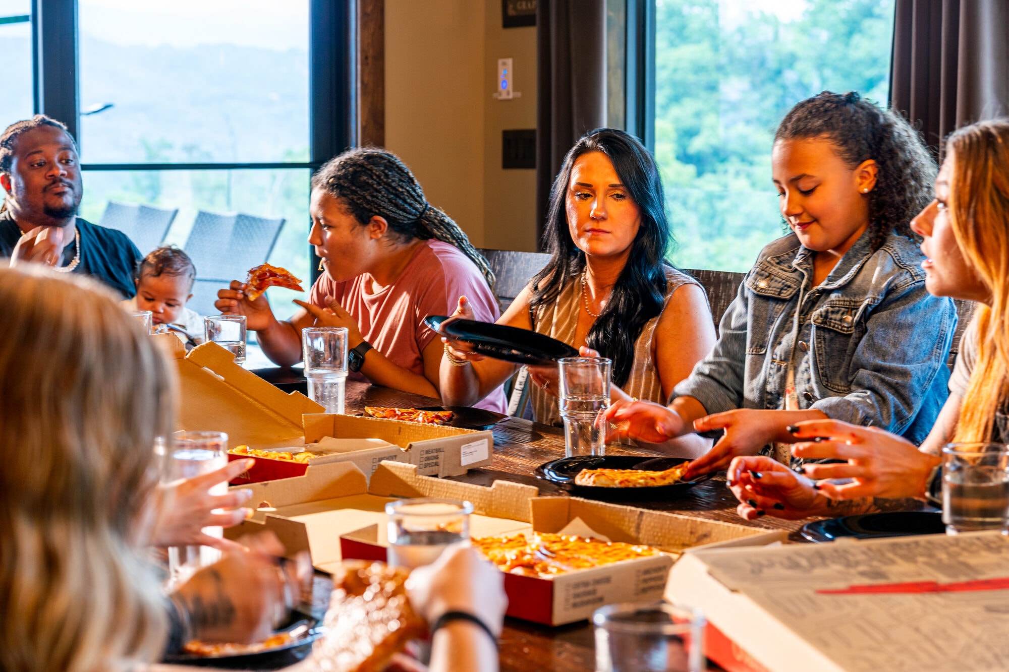 Diverse group eating pizza together indoors, family reunion dinner